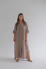 Camisola larga a rayas verticales color café, confeccionada en lino 100%. Tiene cuello camisero, mangas largas con botón ajustable y cierre frontal con botones.