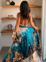 Vestido largo de tela fluida, color verde esmeralda con estampado abstracto en tonos turquesa y detalles dorados. Diseño asimétrico con un solo tirante tejido en el hombro.