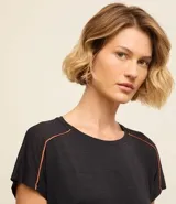 Remera deportiva negra de manga corta confeccionada en microfibra de poliamida ligera con agujeritos en los hombros y bieses en contraste color naranja en las sisas.