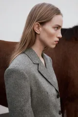 Blazer gris jaspeado de cuello solapa y manga larga con hombreras. Tiene bolsillos delanteros con solapa y cierre frontal cruzado con botones.