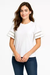 Remera blanca de algodón con cuello redondo, mangas cortas abullonadas con detalle de encaje calado y corte holgado.