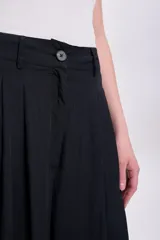 Pantalón negro de corte palazzo con pinzas en la cintura, bolsillos laterales y cierre frontal con botón.