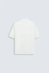 Camisa de calce relajado confeccionada en tejido fluido de mezcla de viscosa, color blanco. Presenta cuello bowling, manga corta, aberturas laterales en el bajo y cierre frontal con botones al tono.