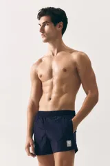 Short de baño azul marino de nylon con elástico revestido y cordón para ajustar oculto en la cintura, bolsillos laterales y bolsillo de solapa con cierre autoadherente atrás. Largo por encima de la rodilla con abertura corta en los laterales y suspensor interior en malla suave.