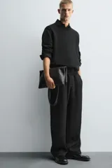 Pantalón negro de corte relajado con cintura elástica ajustable y pliegues en la parte delantera. Presenta bolsillos laterales y bolsillos traseros de parche.