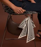 Cartera baguette pequeña de material sintético color marrón, sin estampa, con correa de mano y cierre de cremallera. No incluye pañuelo.