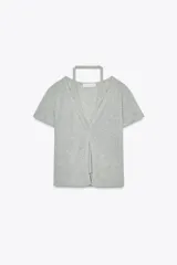Camiseta color beige de tejido de punto, con cuello halter y escote pico. Tiene cierre frontal con botones y mangas cortas.