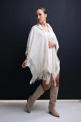 Poncho tejido color crudo con capucha, diseño calado en los bordes y flecos.