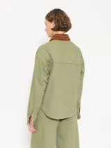 Chaqueta verde militar de algodón con cuello marrón de pana, cierre frontal con botones dorados, bolsillos plaqué en la parte superior e inferior y corte holgado.