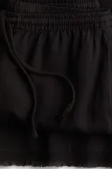 Pantalón negro de corte ancho, confeccionado en mezcla de lino y viscosa. Presenta cintura elástica con cordón ajustable, bolsillos laterales y terminación desflecada en el ruedo.