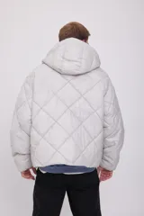 Campera puffer de hombre color gris claro, con capucha ajustable con cordón, cierre de cremallera frontal, bolsillos laterales y mangas largas. Tejido acolchado resistente al viento.