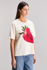 Remera color crudo de calce oversize, confeccionada en tejido jersey 100% algodón. Tiene cuello redondo, manga corta y estampa de una frutilla mordida.