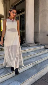 Vestido largo sin mangas, color blanco roto, confeccionado en tejido de red con trama abierta. Se lleva sobre una prenda interior blanca ajustada.