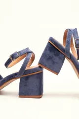 Sandalia de terciopelo verde con taco cuadrado de 7 cm, punta cuadrada y tiras anchas anudadas en el empeine. Cuenta con una tira fina ajustable al tobillo con hebilla dorada.