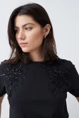 Remera negra de manga corta con apliques bordados en el escote.