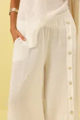 Pantalón palazzo de lino color blanco, con cintura elastizada y botones decorativos en los laterales.