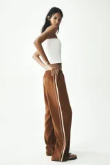 Pantalón marrón de tiro alto con cintura elástica, bolsillos delanteros y detalle de banda lateral blanca a contraste.