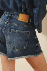 Short de jean de tiro medio, confeccionado en denim rígido azul, con lavado localizado con bigotes y ruedo desflecado.