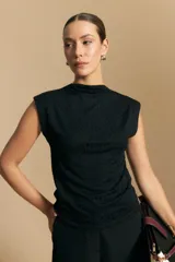 Top sin mangas negro, con cuello alto y hombros ligeramente estructurados. El tejido presenta una textura sutil con brillo integrado que simula un animal print.