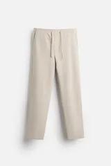 Pantalón de jogging color beige confeccionado en tejido de mezcla de algodón. Cuenta con cintura elástica ajustable con cordón, bolsillos frontales y traseros.
