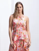 Vestido largo de gasa estampada con flores en tonos naranja, rosa y lila. Tiene escote halter, busto plisado, corte en la cintura con faja plisada y falda con sobrecapa y forro interno a tono.