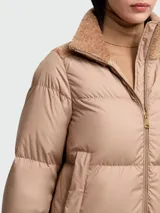 Campera de plumas corta, color beige, con cierre frontal y cuello alto de tejido tipo borrego en tono camel. Presenta hombros y cuello con apliques de borrego.