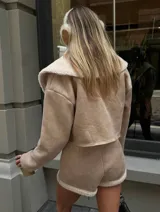 Conjunto color beige compuesto por chaqueta corta con cuello de piel sintética y short con cierre frontal.