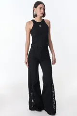 Pantalón de jean negro de pierna ancha con cortes en los laterales que van desde la pretina al bajo del pantalón. Por la mitad de la pierna presenta godets triangulares de encaje para darle mayor amplitud y detalles a la prenda.