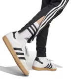 Pantalón de jogging negro con tres rayas blancas a los costados y logo de Adidas en la pierna izquierda.
