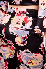 Conjunto de pantalón y top de viscosa con estampado floral en tonos rosa, celeste, amarillo y rojo sobre fondo negro. El top es cruzado con mangas acampanadas y el pantalón es de corte palazzo con cintura elastizada.