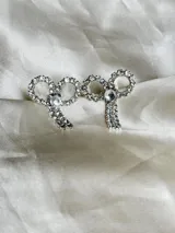 Par de aros colgantes con forma de moño, con engarce de strass y gancho de acero quirúrgico.