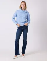 Buzo de punto grueso color beige, con cuello volcado y textura en relieve. Tiene mangas largas de corte hombro caído y puños anchos.