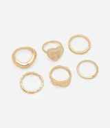 Set de seis anillos dorados con diferentes diseños: uno liso, uno con textura, uno con forma de corazón esmaltado con moño, uno con pequeñas piedras incrustadas y dos anillos lisos finos.