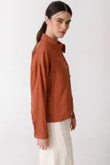 Blusa blanca de lino con cuello polo, manga larga y botones dorados. Presenta costuras a contratono en color naranja.