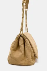 Bolso de hombro color beige, confeccionado en piel de serraje. Tiene correa metálica con detalles, pespuntes en el cuerpo, múltiples bolsillos con cierre de cremallera metálica, cierre imantado y solapa.