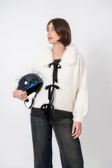 Cardigan blanco de lana con cuello de piel sintética, cierre frontal con lazos de terciopelo negro y corte holgado.