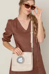 Cartera de mano tipo sobre, color beige claro, con solapa frontal decorada con una piedra de ágata azul engarzada en metal plateado. Posee correa larga ajustable de cuero beige.