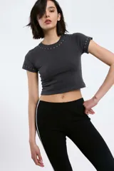 Remera blanca de algodón con cuello redondo y mangas cortas, con detalle de tachas plateadas en cuello y mangas.