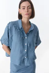 Camisa color beige de lino con cuello camisero, manga corta y cierre frontal con botones. Presenta detalles de encaje en el cuello, el frente y las mangas.