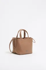 Bolso tote pequeño color visón de piel granulada con doble asa corta y correa bandolera ajustable y extraíble. Incluye bolsa interior ajustable con cordones. Logotipo de la marca grabado en el frente.