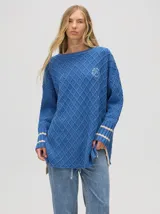 Sweater color crema con tejido en ochos, cuello redondo, puños acanalados con doble raya azul y tajos a los costados.