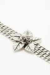 Pulsera metálica plateada con cadenas de eslabones gruesos y flor central con textura y detalles de strass.