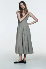 Vestido midi de tirantes con escote cuadrado y falda amplia con godets, confeccionado en tela con estampado de cuadros vichy en blanco y negro.