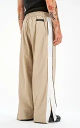 Pantalón deportivo beige de nylon con cintura elástica ajustable con cordón, corte holgado y aberturas laterales con broches.