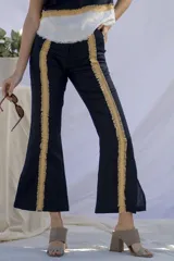 Pantalón de lino negro con corte acampanado y detalle de flecos dorados en los laterales.