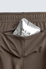 Pantalón corto deportivo color marrón oliva, con cintura elástica ajustable con cordón, bolsillos frontales y bolsillo trasero con cierre. Presenta forro interior y detalle de logo estampado en la pernera.
