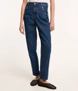 Pantalón mom confeccionado en jeans azul con trabillas en la cintura, cierre tradicional por botón y cremallera, bolsillos delanteros y traseros con detalle deshilachado.