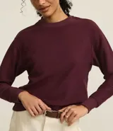 Sweater color borgoña de algodón con poliéster, cuello redondo y mangas largas con puños acanalados.