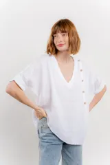 Blusa color naranja confeccionada en 100% lino, con escote en V, mangas cortas con vuelta y silueta amplia. Presenta terminación asimétrica y fila de botones decorativos en uno de los hombros.