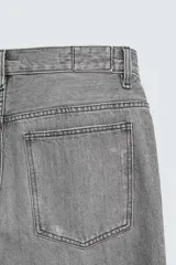 Bermuda de denim de algodón, color gris lavado, con corte relaxed fit y roturas visibles en la parte delantera de ambas piernas. Presenta cinco bolsillos y cierre frontal con cremallera y botón.